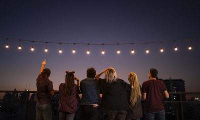 Friends spending leisure time under string lights on rooftop at dusk