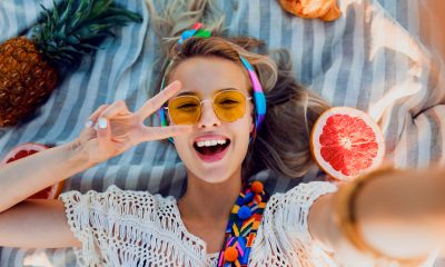 Excited girl making selfie on beach towel. Boho accessories. Yellow sunglasses.Top view.
