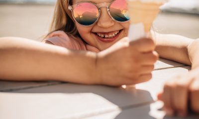 Beautiful girl holding a ice cream over a beach boardwalk. Young girl wearing sunglasses at the beach eating icecream on a summer day.